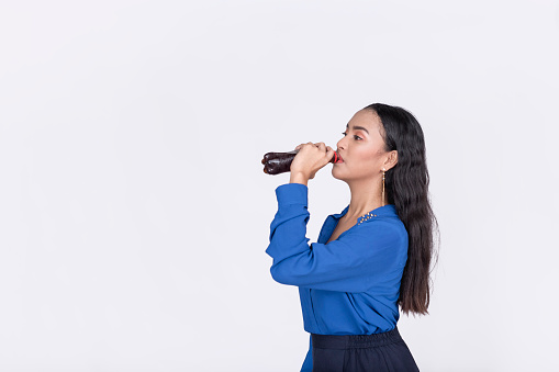 A young office employee chugs down a bottle of cola for refreshment. Isolated in white backdrop.