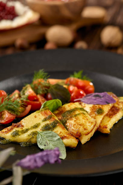 istock Grilled halloumi cheese with pesto sauce and tomatoes on black plate. Appetizer from fried cheese in greek style on wooden background. Hot appetizer of halloumi cheese in rustic style. 1407836048