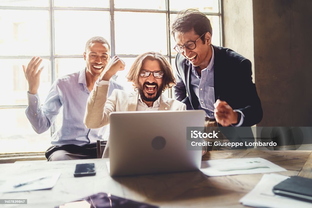 Cheerful excited businessmen guys celebrating their success. Winners, multi-ethnic people reading good news online on laptop screen - lifestyle business people concept Business Stock Photo