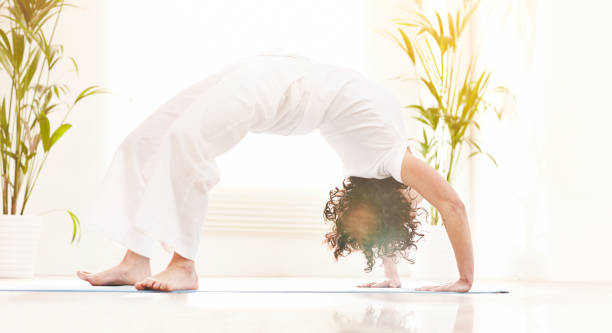 istock Woman in backbend wheel yoga pose and stretching her back during a zen retreat studio class. Yogi balancing alone on mat. Finding inner mental balance and peace with calming, holistic body exercise 1407842343