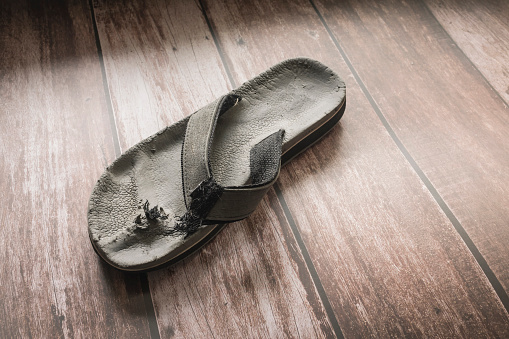 An old damaged sandal on the floor. Toe post torn and ripped off by a dog. Copyspace.