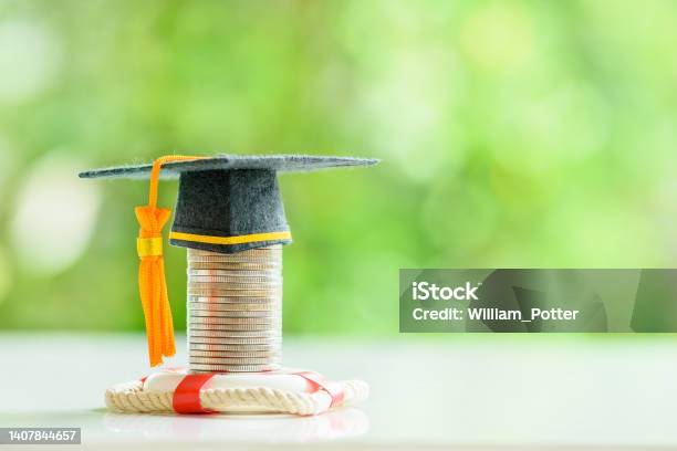 Tuition Protection Service And Tuition Refund Insurance Financial Concept Black Graduation Cap Or A Mortarboard Placed Higher On Top Of A Coin Stack With A Red Lifebuoy On A Table Stock Photo - Download Image Now
