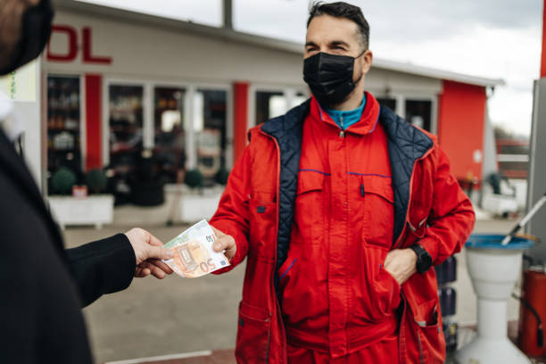 Gas station work Young handsome adult man paying the bill with a cash. Thea are wearing protective face masks against virus pandemic. cash for cars stock pictures, royalty-free photos & images