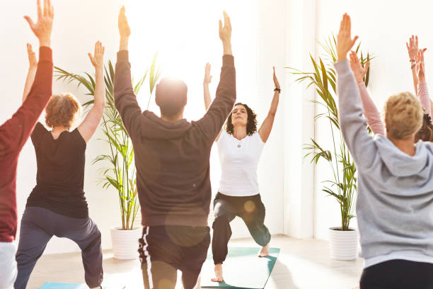 istock Yoga instructor training people during a fitness class in a studio. Yogi teaching crescent lunge pose with arms outstretched and mindful meditating exercises for zen energy during a group lesson 1407852333