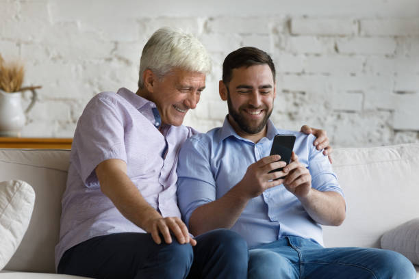 istock Older man his grownup son sit on sofa using smartphone 1407852351
