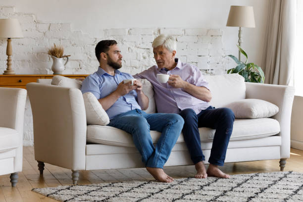 istock Older man grownup son talking seated on sofa with teacups 1407852733
