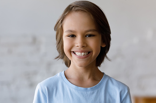 Head shot portrait front face view of handsome 9s boy having wide toothy smile looking at camera standing alone indoor. Generation Z, pre-adolescence, dental clinic services for little clients concept
