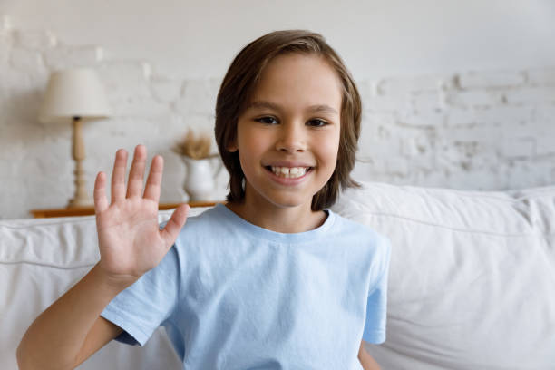 istock Cute little boy sit on couch wave hand start videocall 1407852748