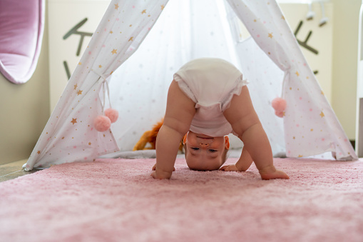 Cute baby girl standing upside down on the carpet in the bedroom