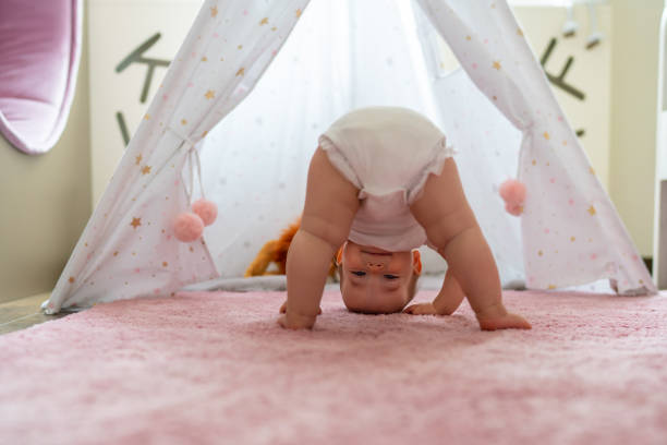 Happy baby girl standing upside down on the carpet at home stock photo