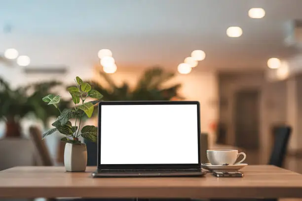 Mockup of laptop computer with empty screen with coffee cup and smartphone on table of the coffee shop background,White screen