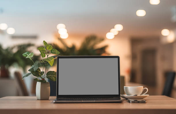 istock Mockup of laptop computer with empty screen with coffee cup and smartphone on table of the coffee shop background,Gray black screen 1407857879