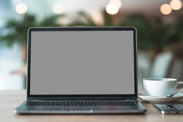istock Mockup of laptop computer with empty screen with coffee cup and smartphone on table of the coffee shop background,Gray black screen 1407857994