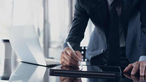 istock Asian businessman using stylus pen signing e-document on digital tablet with laptop computer on table at office, e-signing, electronic signature, paperless office 1407858193