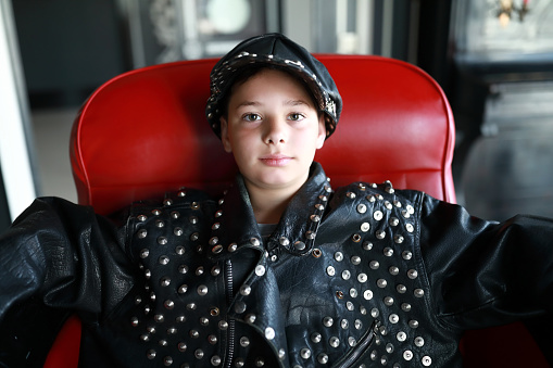 Portrait of child in leather jacket and cap sitting on chair