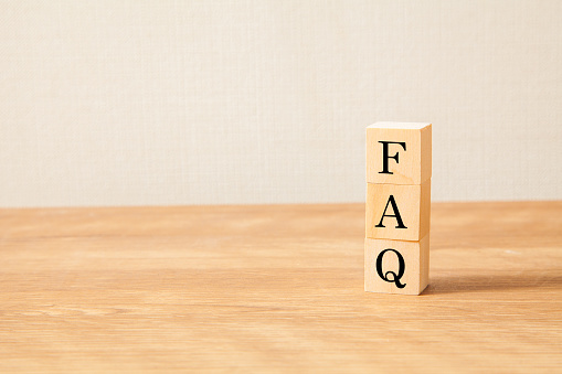 FAQ text. Frequently Asked Questions. Frequently Asked Questions. Written on three wooden blocks. Wooden table and white wallpaper background. Copy space on the left.