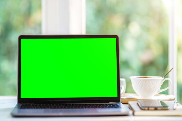istock Mockup of laptop computer with empty screen with notebook,coffee cup and smartphone on table side the window in the coffee shop at the cafe,Green screen 1407859427
