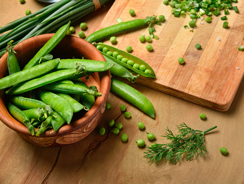 vegetables on a wooden kitchen board, sliced green onions, dill and peas on a wood background, concept of fresh and healthy food, still life