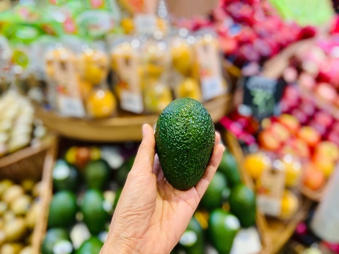 hand holding Avocado Blurry fruits background in supermarket