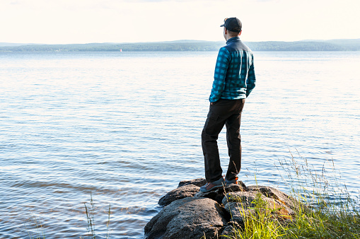 young man in a cap looking at the view of the lake or river standing on the stones Enjoying nature landscape