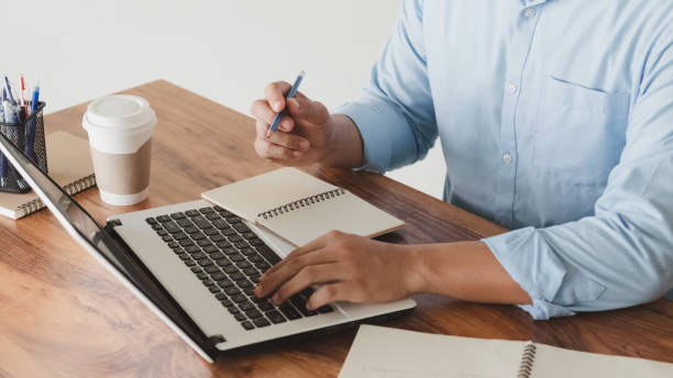 istock young man using laptop computer and mobile phone When looking for financial information in business, work at the desk. Writing with a pen, studying remotely from home and working from home. 1407863415