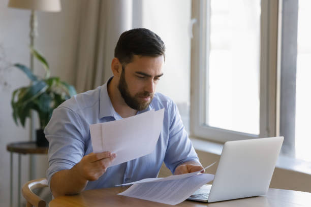 istock Serious man sit at table with laptop sorting out papers 1407865346