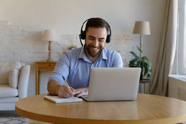 istock Man sit at desk with laptop makes notes in copybook 1407865356