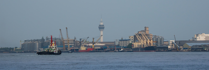 A view of a river with pilot boats at work. Ports, industrial sites, and expanding cities may be seen in the backdrop.