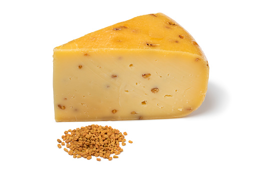 Piece of Gouda cheese with  Fenugreek and a heap of seeds in front  isolated on white background close up