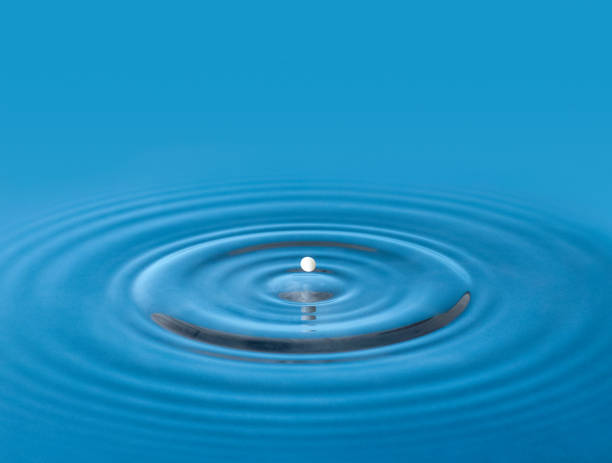 istock Splash of a white round drop in blue water with circles 1407867625