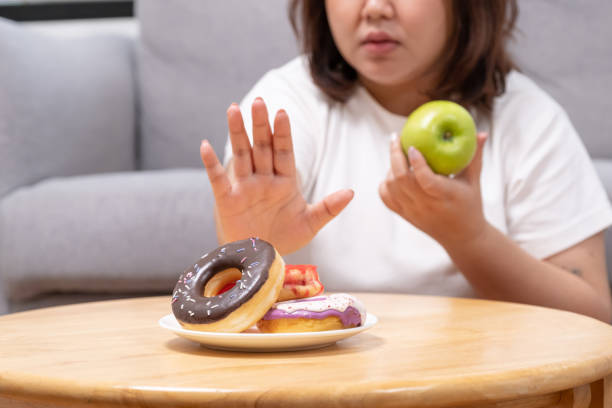 istock Selective focus at donut. Young beautiful, say no or refuse to eat donut  which can cause overweight or health problem. Junk food that can cause obesity and unhealthy for human body. 1407870604