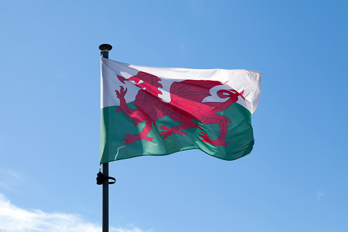 Flag of Wales waving atop of its pole against a blue sky.