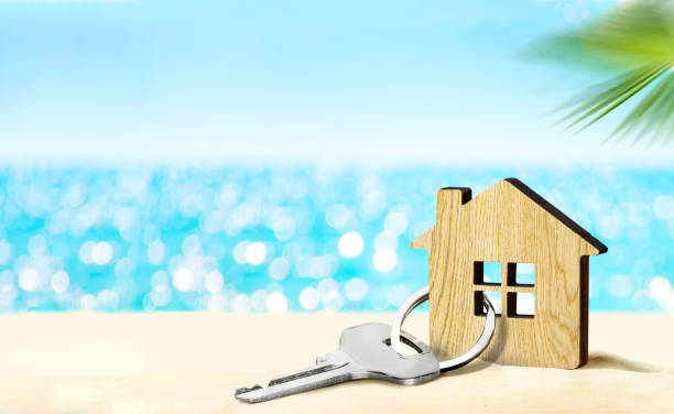 House by the sea concept. Figure of house and key on sandy beach Model of house and key on sandy beach with sea and sky on the background vacation rental stock pictures, royalty-free photos & images