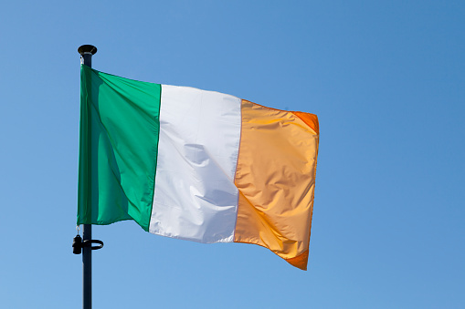 Flag of Ireland waving atop of its pole against a blue sky.