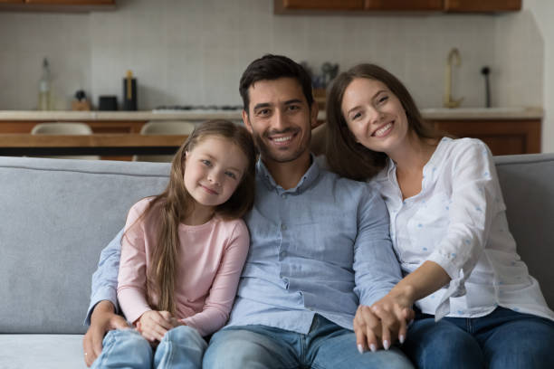 istock Couple and daughter smile look at camera seated on sofa 1407878133