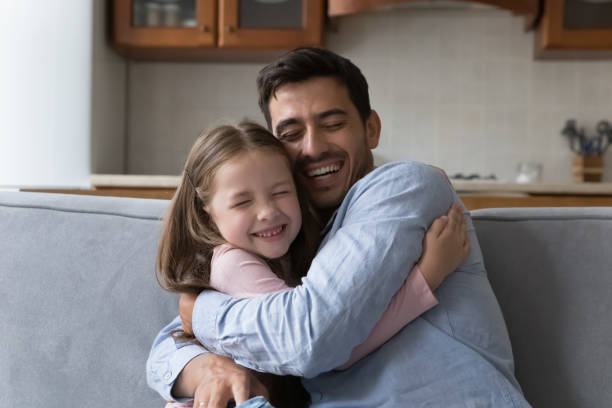 istock Little daughter cuddles tightly her stepdad seated on sofa 1407878142