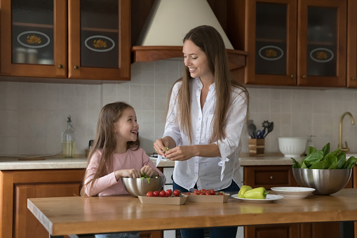 Young mother teach her little cute daughter to cook. Parent caring about health, cooking balanced natural dietary food, prepare together with child vegetarian dish in kitchen at home. Cookery concept