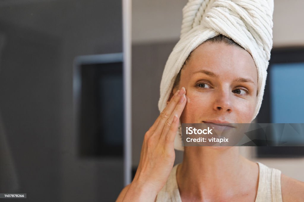 Woman Applying Moisturizing Face Cream Woman applying face cream in front of a mirror Face Cream Stock Photo