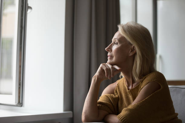 istock Pensive aged female resting on sofa looking out window 1407878360