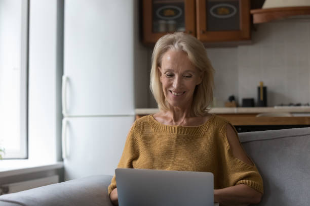 istock Smiling older woman using laptop at home 1407878378