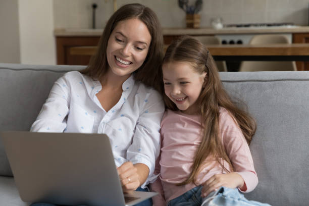 istock Young mother and little daughter sit on sofa using laptop 1407879005