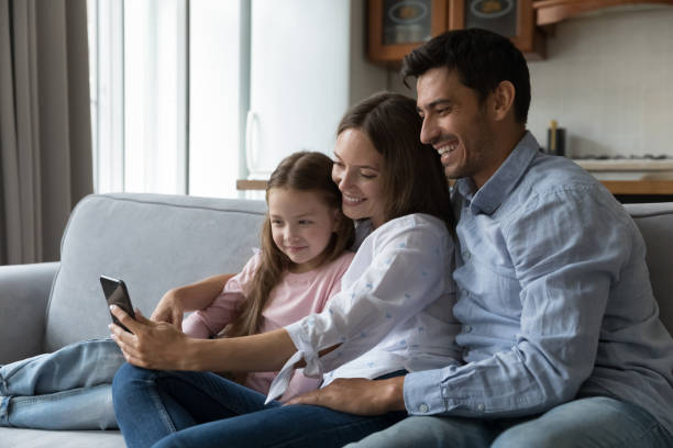 istock Couple with daughter sit on sofa using smartphone 1407879256