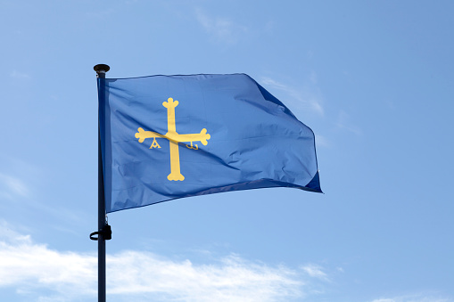 Flag of Asturias (Victory Cross) waving atop of its pole against a blue sky.