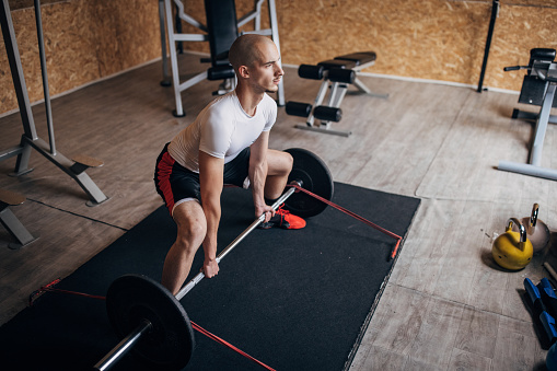 One man, fit young man training with weights in gym alone.