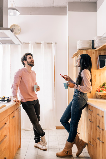 Beautiful black woman and her boyfriend using phone while standing in the kitchen at home.