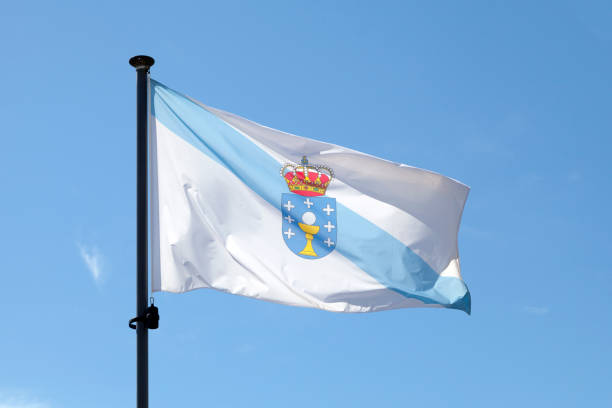 Flag of Galicia waving atop of its pole against a blue sky.