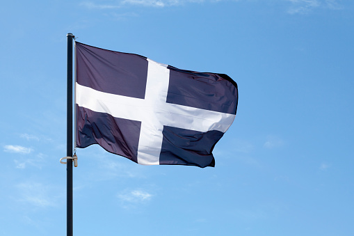 Saint Piran's Flag (Cornwall) waving atop of its pole against a blue sky.