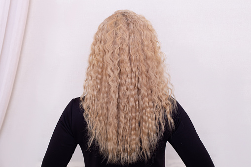 Female back with long curly blonde hair in hairdressing salon