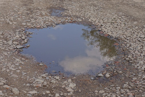 one big puddle with dirty water on gray ground and rubble on the road outside