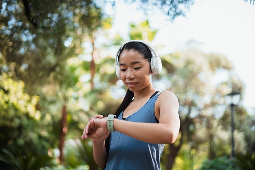 Asian sport girl looking at her smart watch while resting of jogging in the park